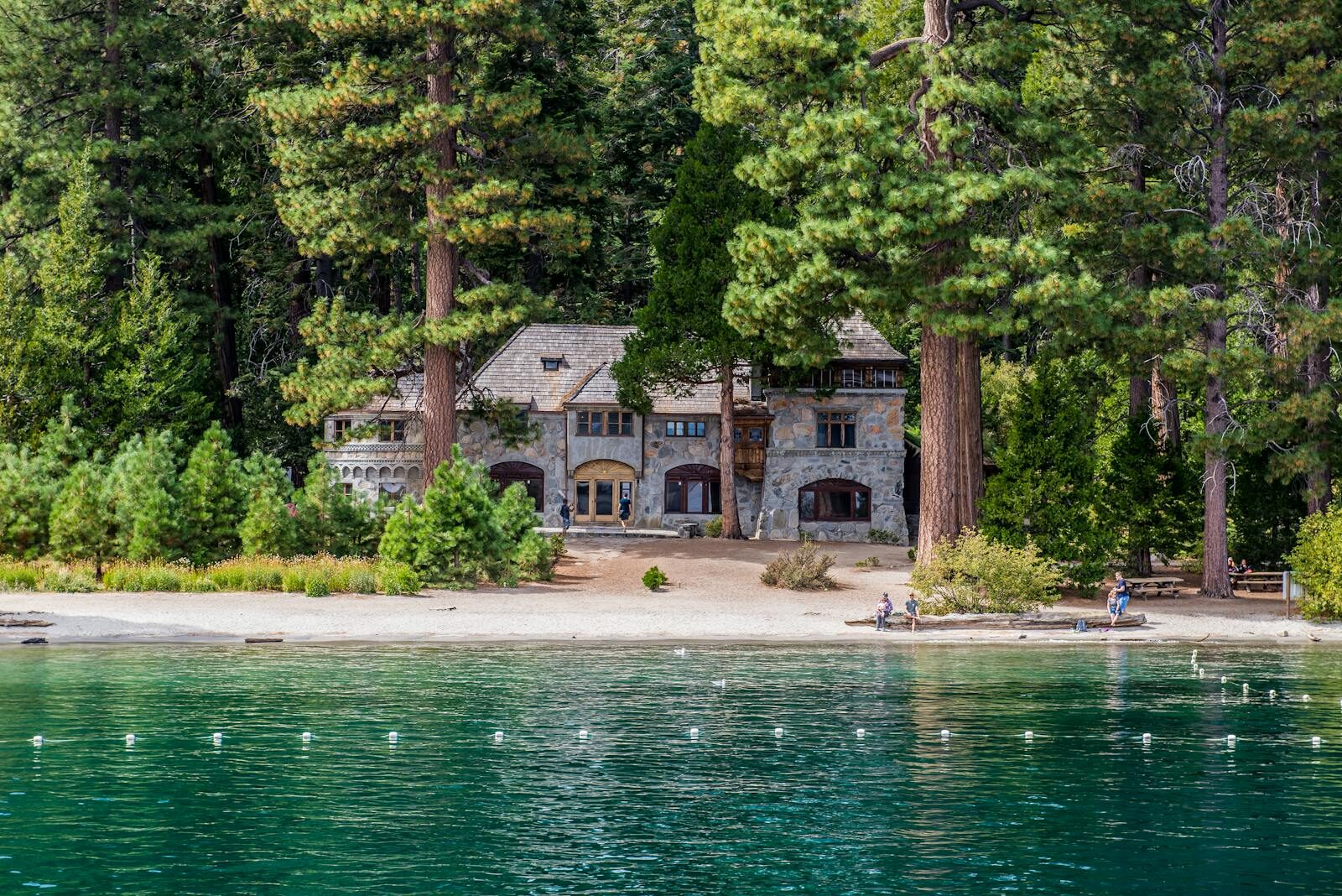 A quaint stone house nestled by a tranquil lakeshore surrounded by lush greenery.
