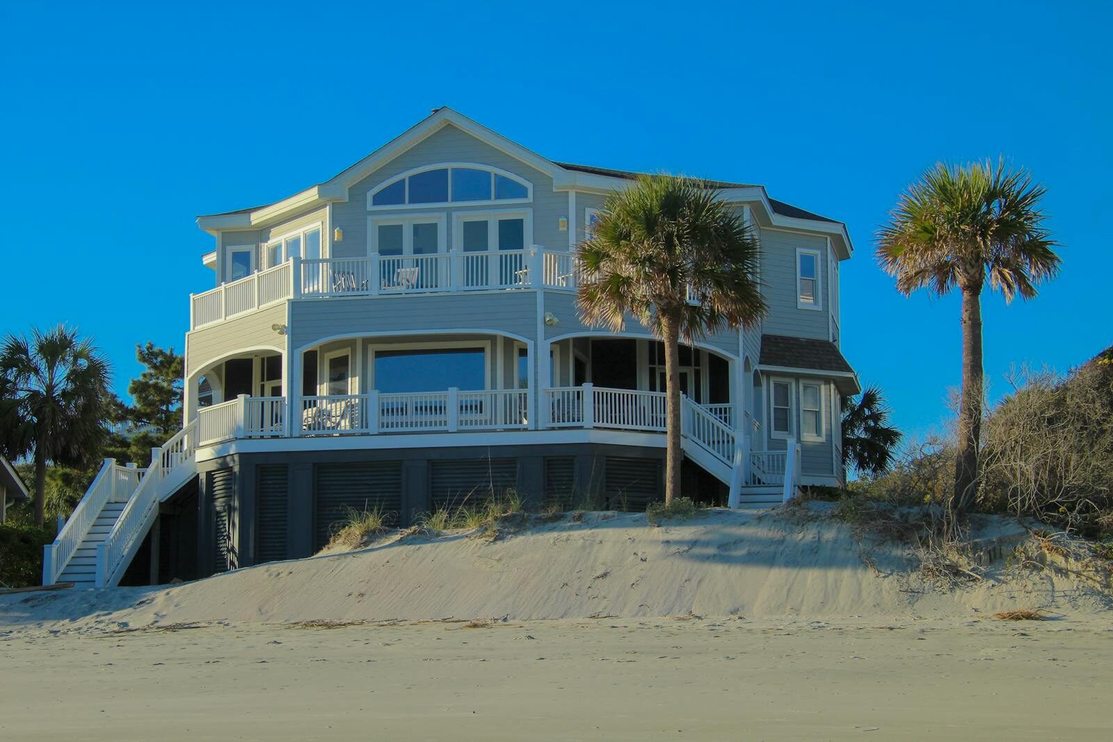 Elegant beachfront house with large windows and palm trees under clear blue sky.