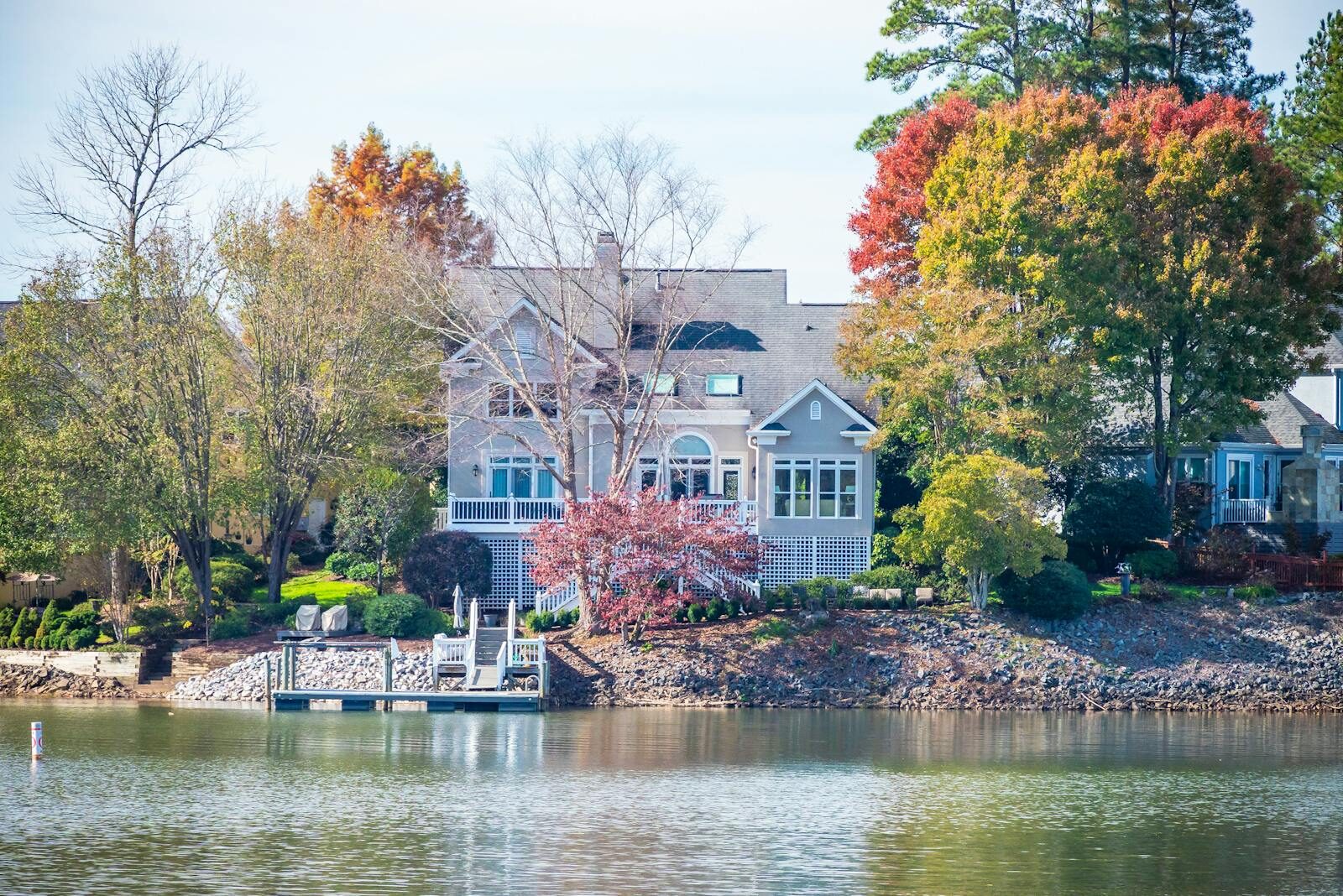 Charming house by the lake surrounded by vibrant autumn trees reflecting on water.