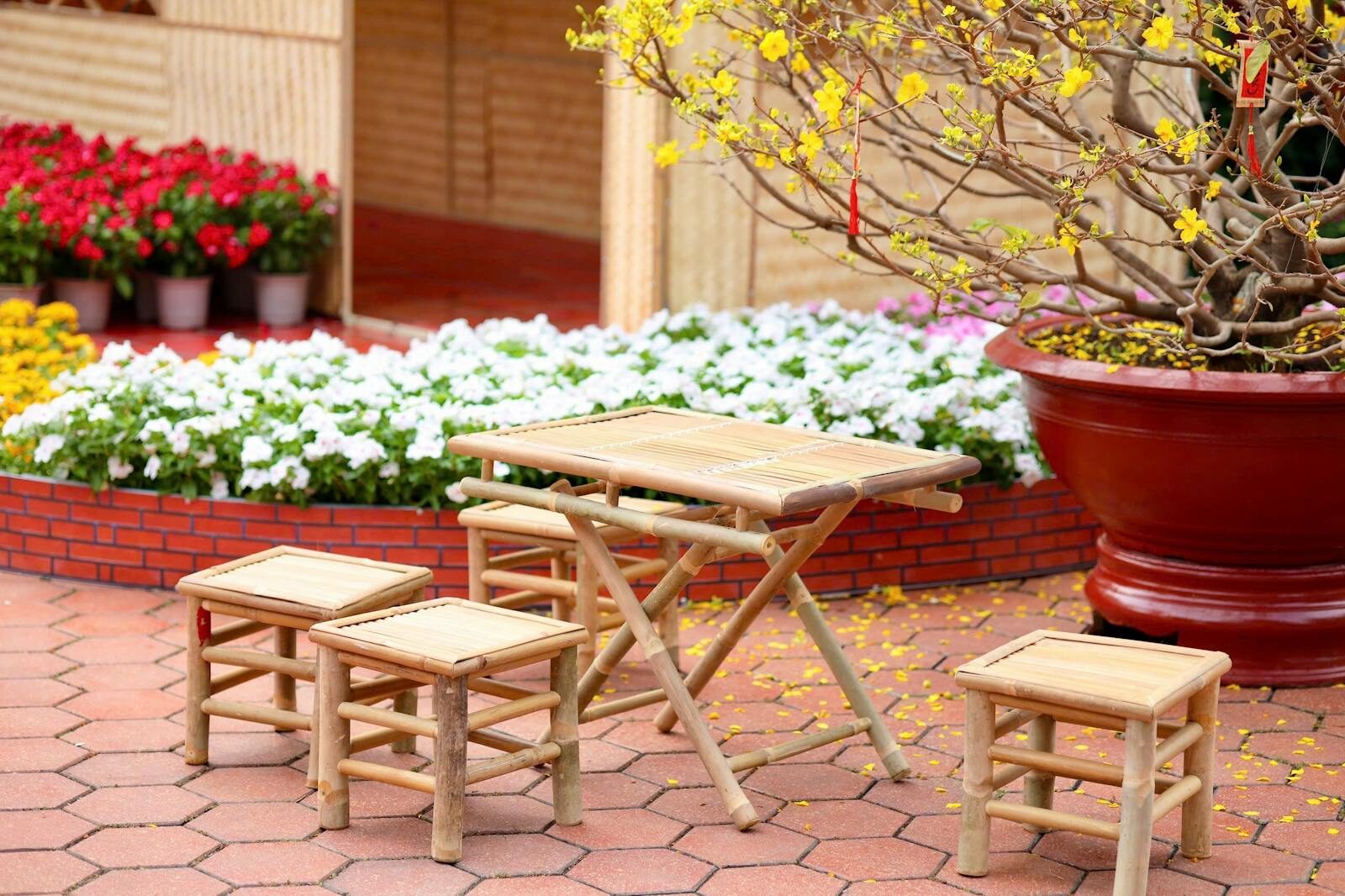 A bamboo table set outdoors in a colorful garden with blooming flowers and potted plants.