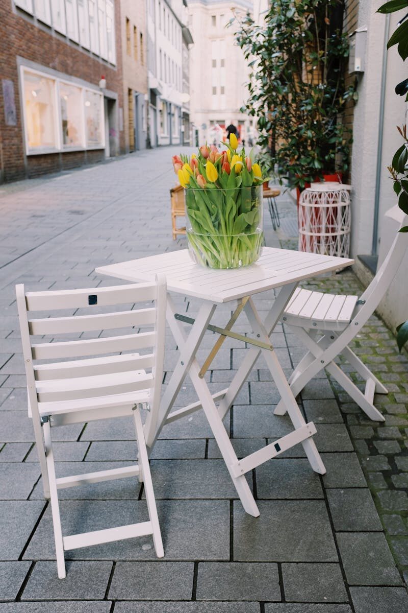 White wooden chairs and table with colorful tulips in vase placed near cafe on street
