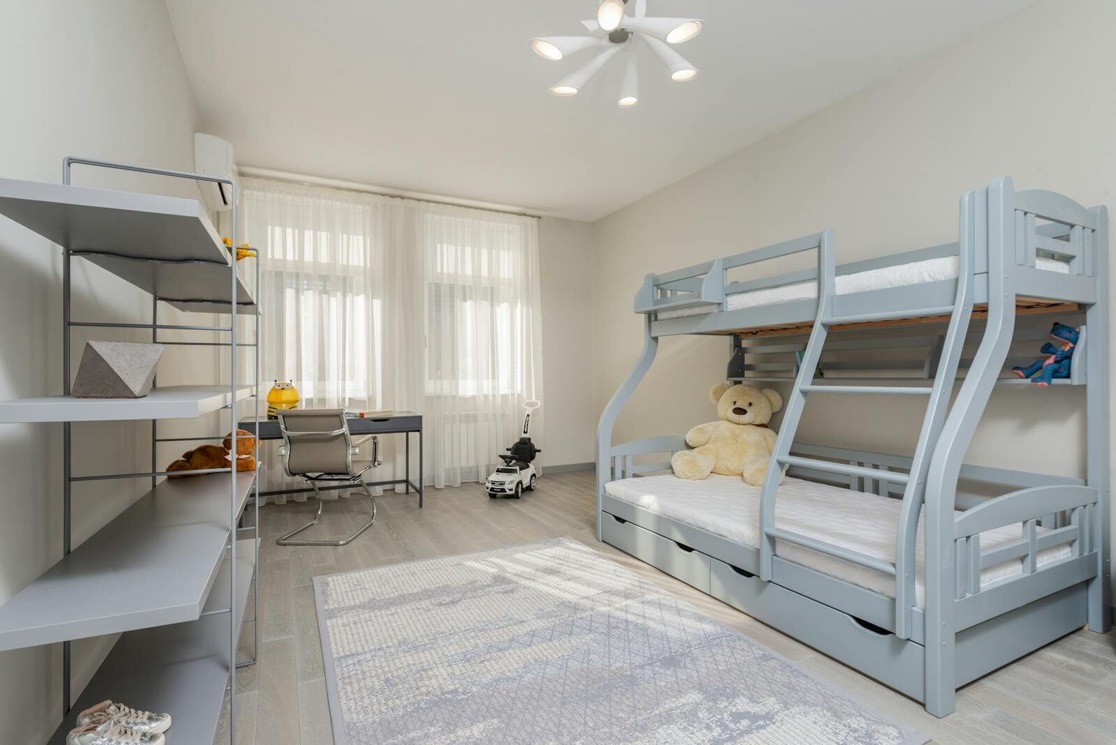 Interior of bedroom with desk and chair near window and gray double deck bed in front of empty shelves