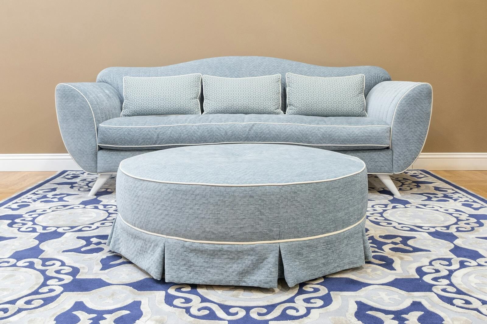 A stylish blue sofa with matching ottoman and decorative rug in a modern living room setting.