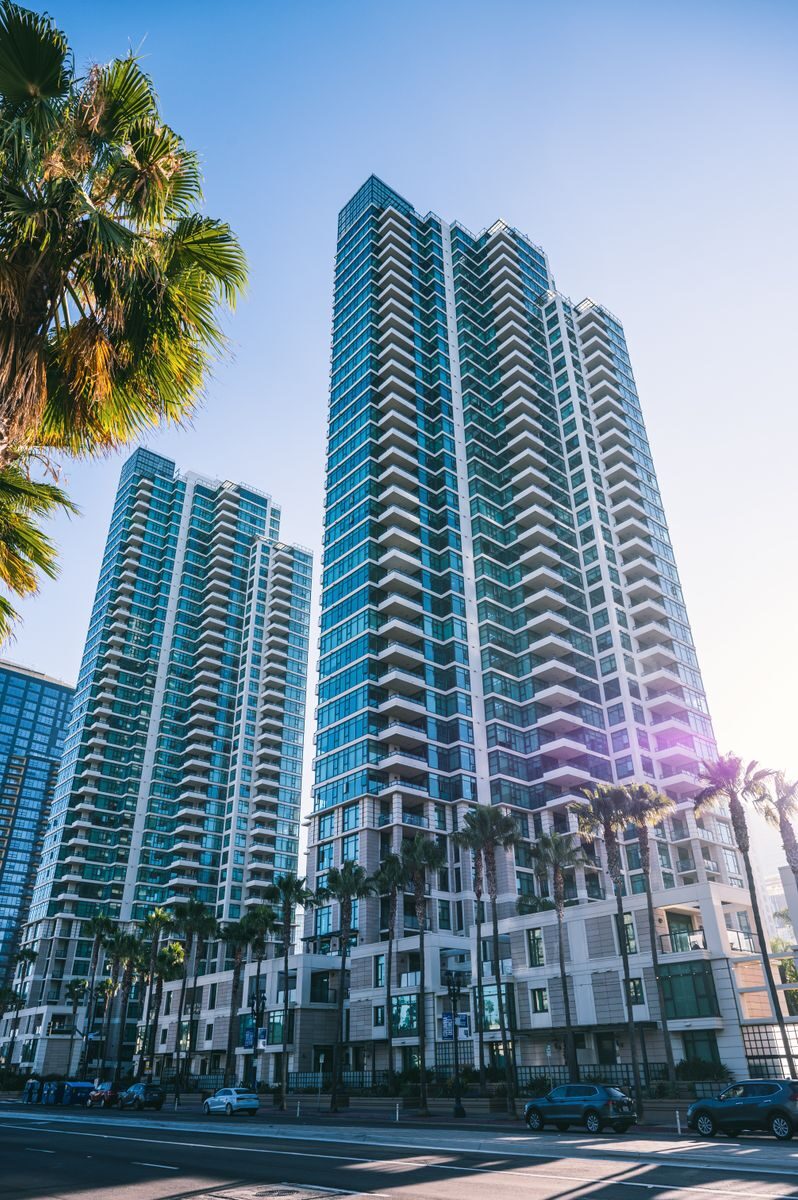 Tall glass skyscrapers against blue sky with palm trees lining the city street, urban architecture.