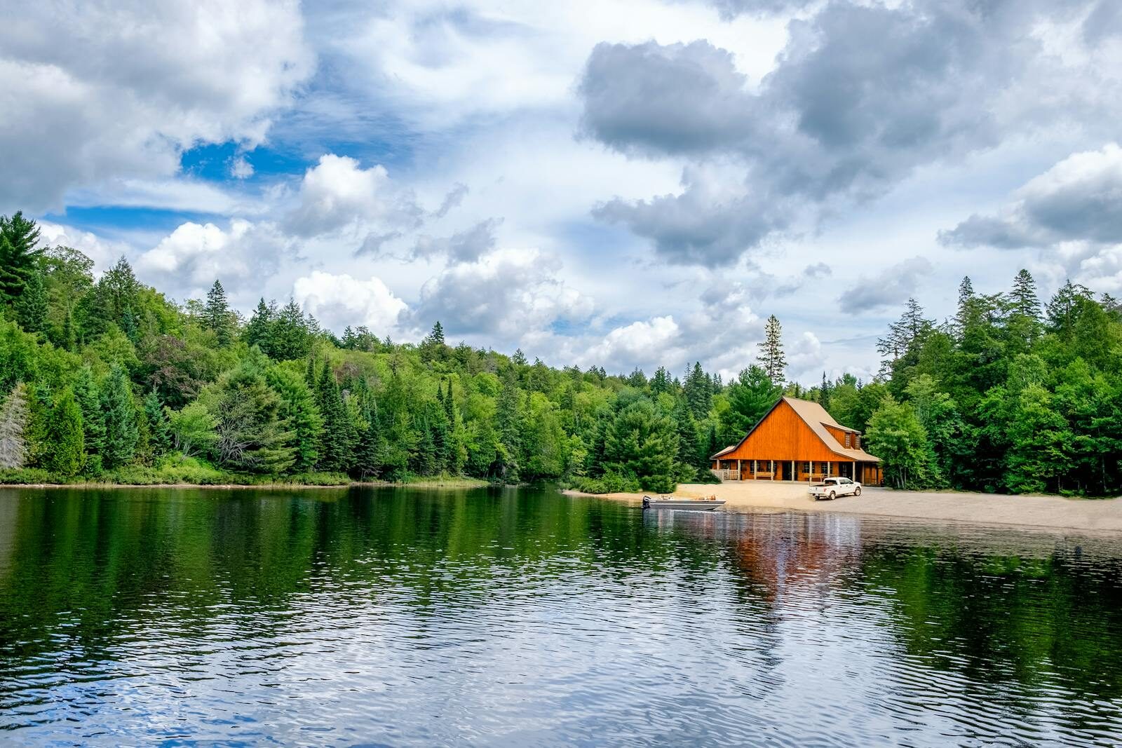 Beautiful lakeside cabin with sandy shore, nestled in lush green forest, under vibrant summer sky.