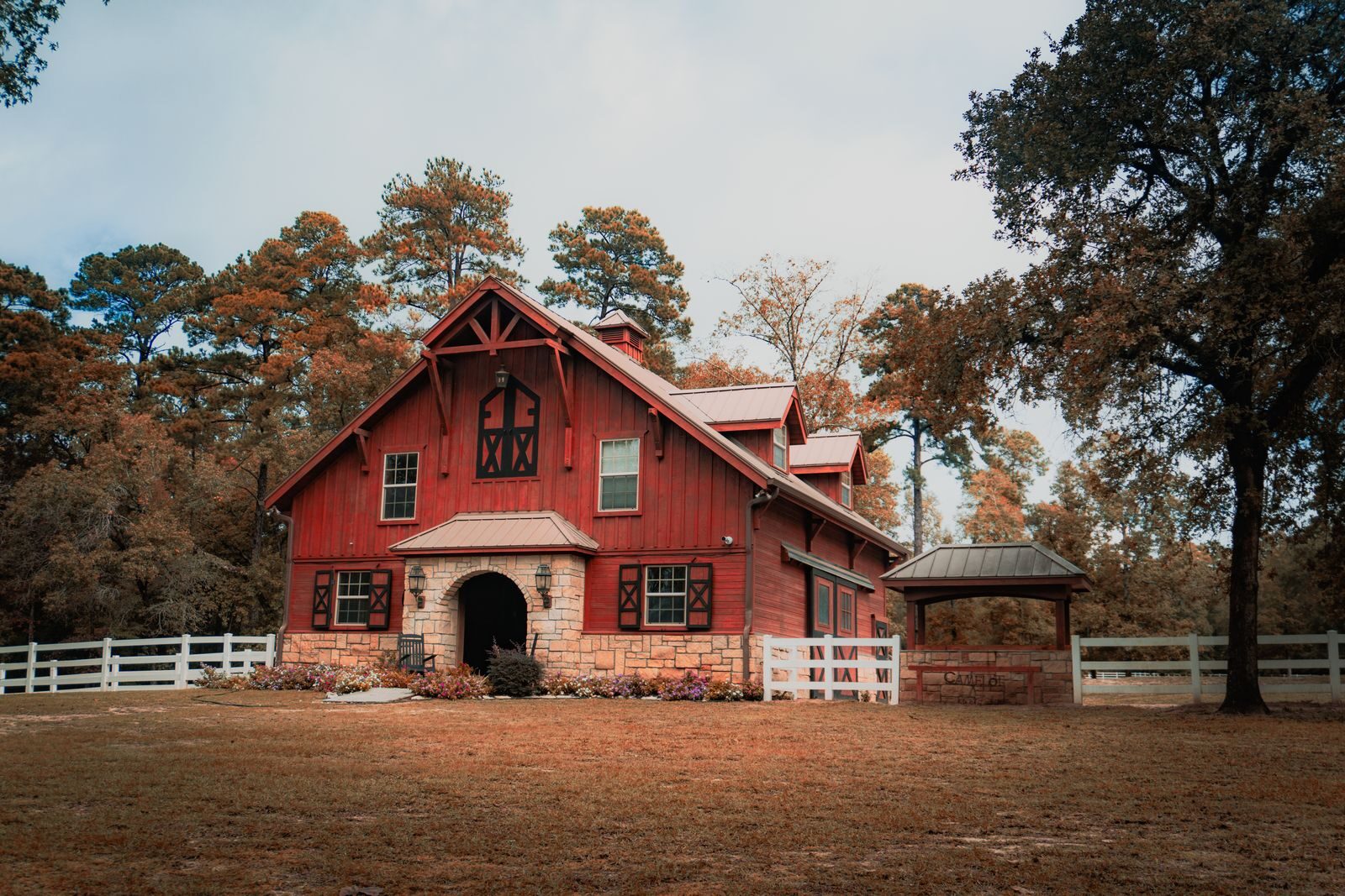 Picturesque red barn surrounded by lush autumn trees and a white fence, capturing serene countryside life.