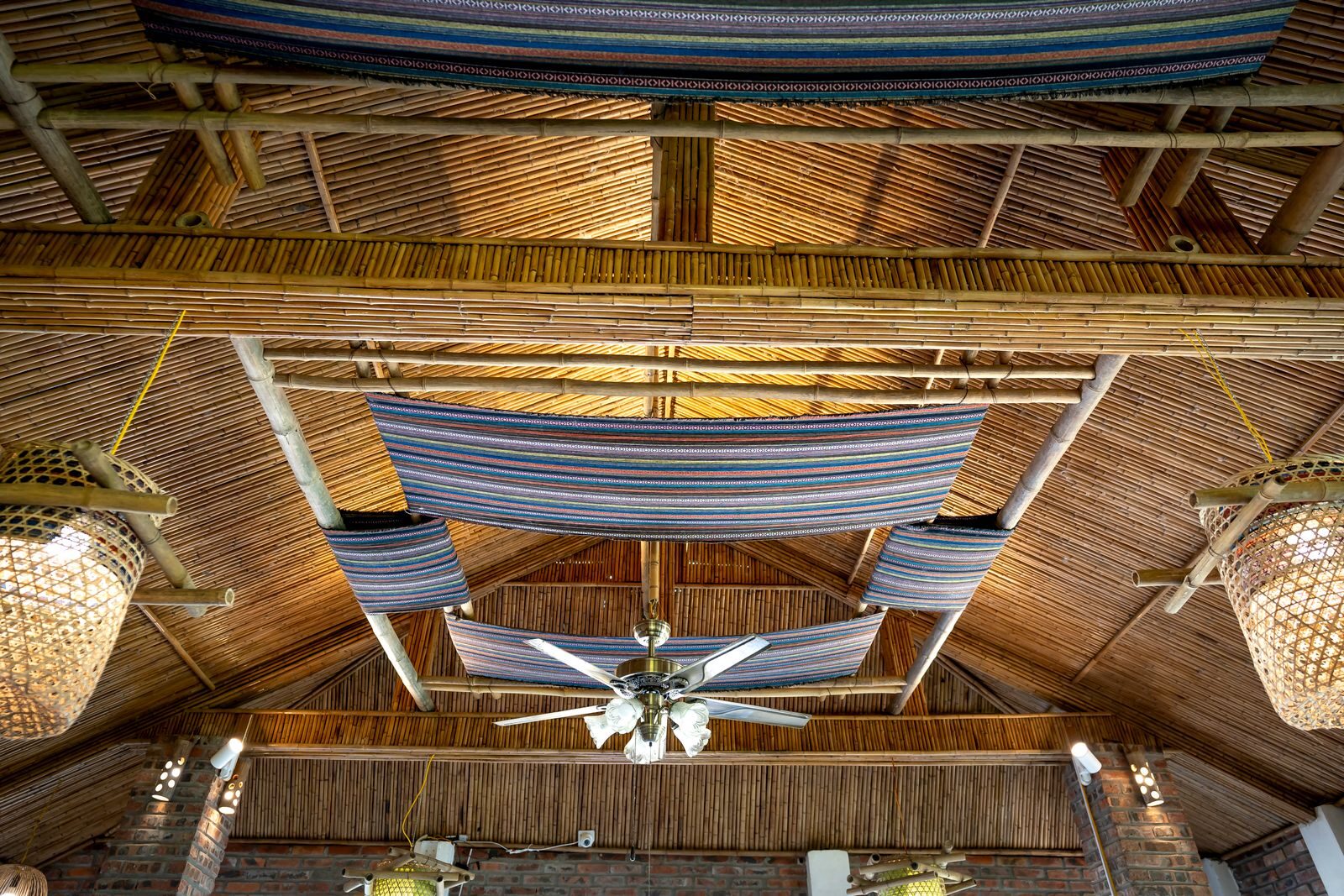 From below of bright chandelier with decorative fabric hanging on wooden roof with glowing lamps in cafeteria of tropical resort