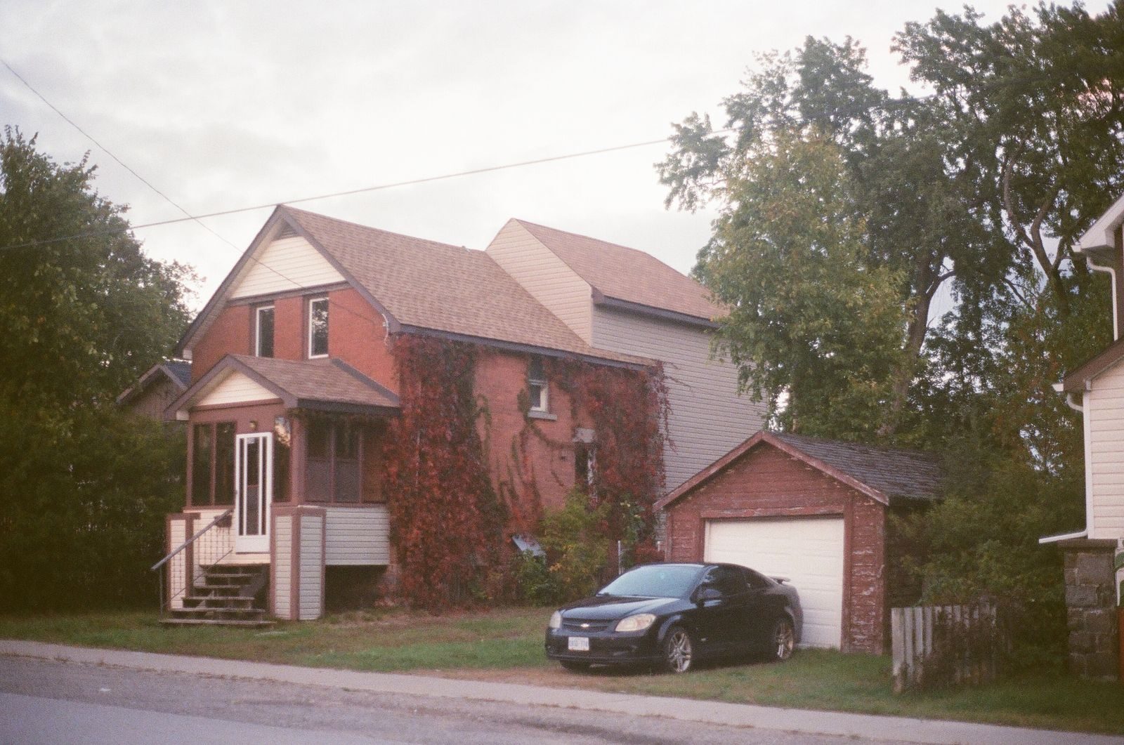 A cozy brick house with a garage and a car parked outside, surrounded by greenery.