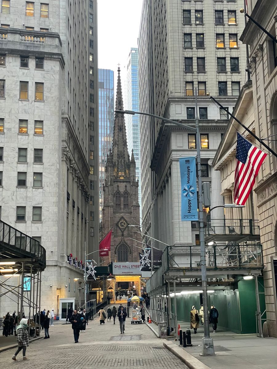 A bustling urban street view in Manhattan featuring the iconic Trinity Church with people and skyscrapers.