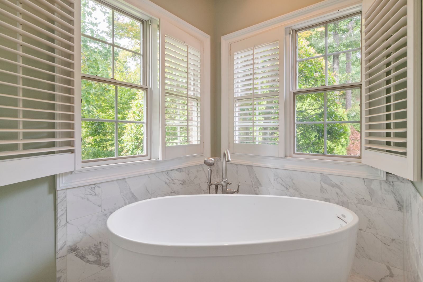 Elegant bathroom featuring a marble design and a freestanding tub, with natural light flooding through large windows.