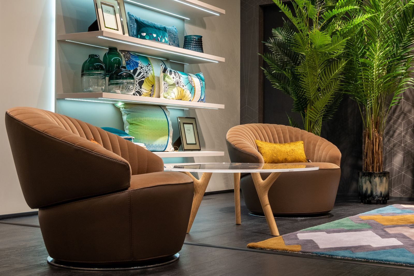 Stylish design of room interior with comfortable armchairs near bright carpet and round glass table against shelves with luminous lights