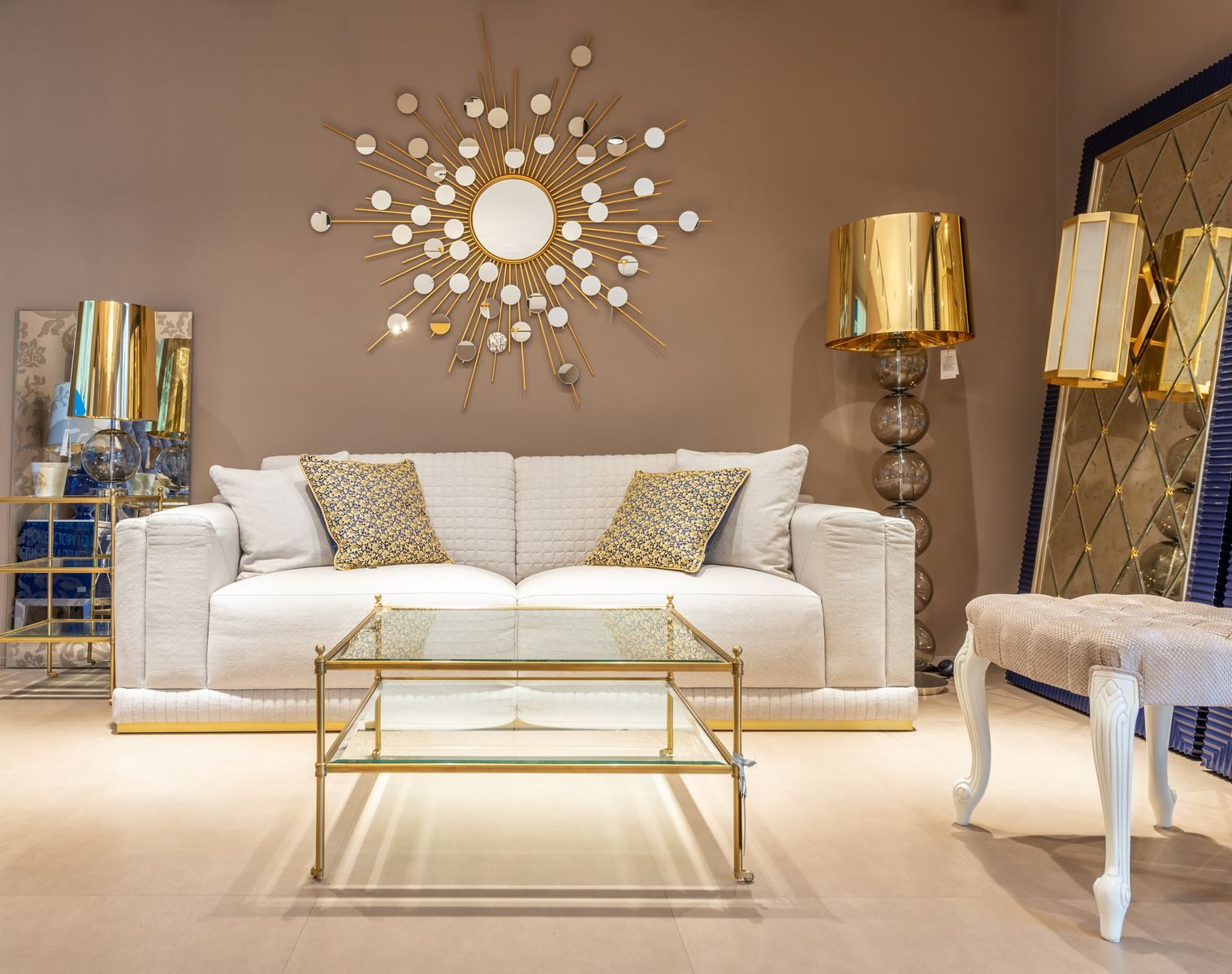 Comfortable white sofa placed near glass table at wall with decorative elements in stylish living room with mirror and table lamp