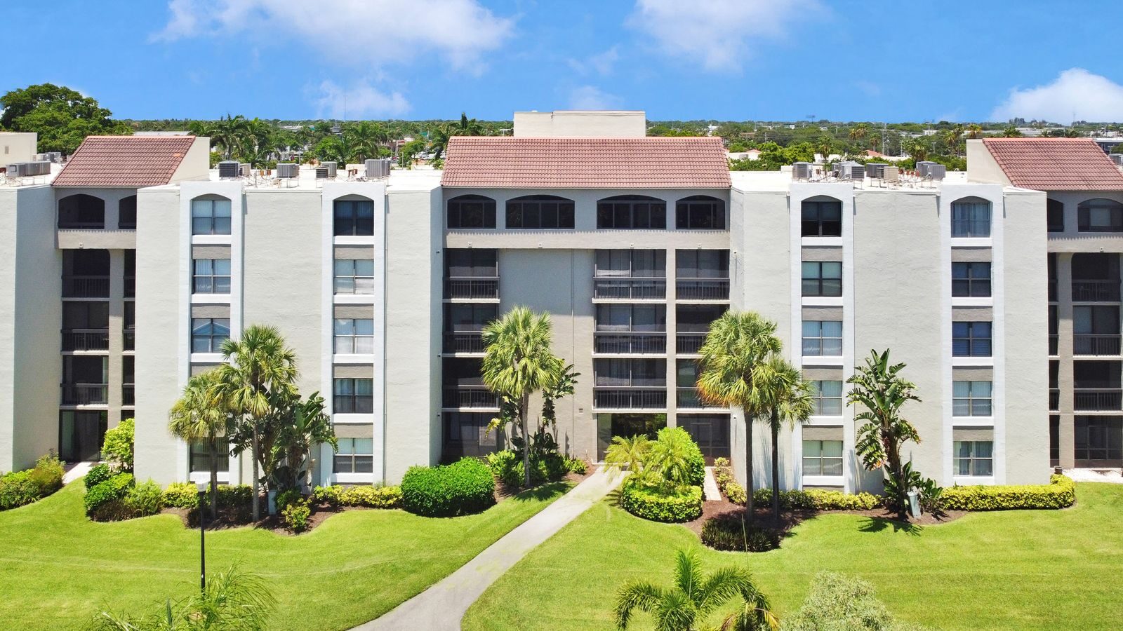 Elegant apartment building surrounded by green lawns and palm trees, perfect for urban living.