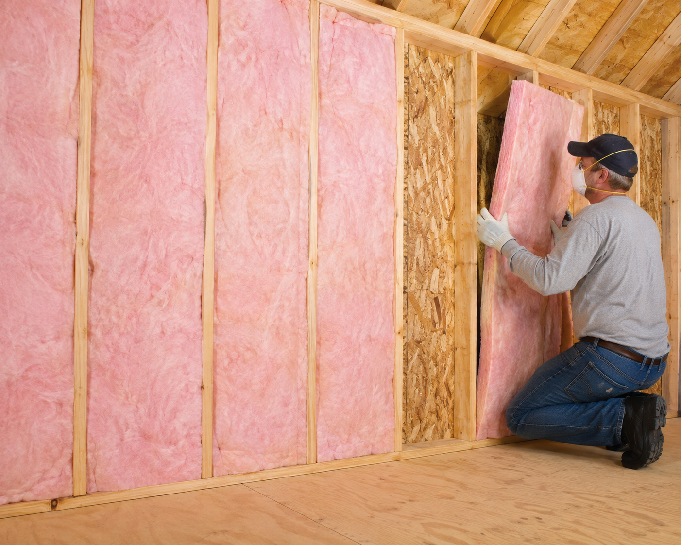 Batt insulation being installed between wood wall studs in a home for improved thermal and energy efficiency.