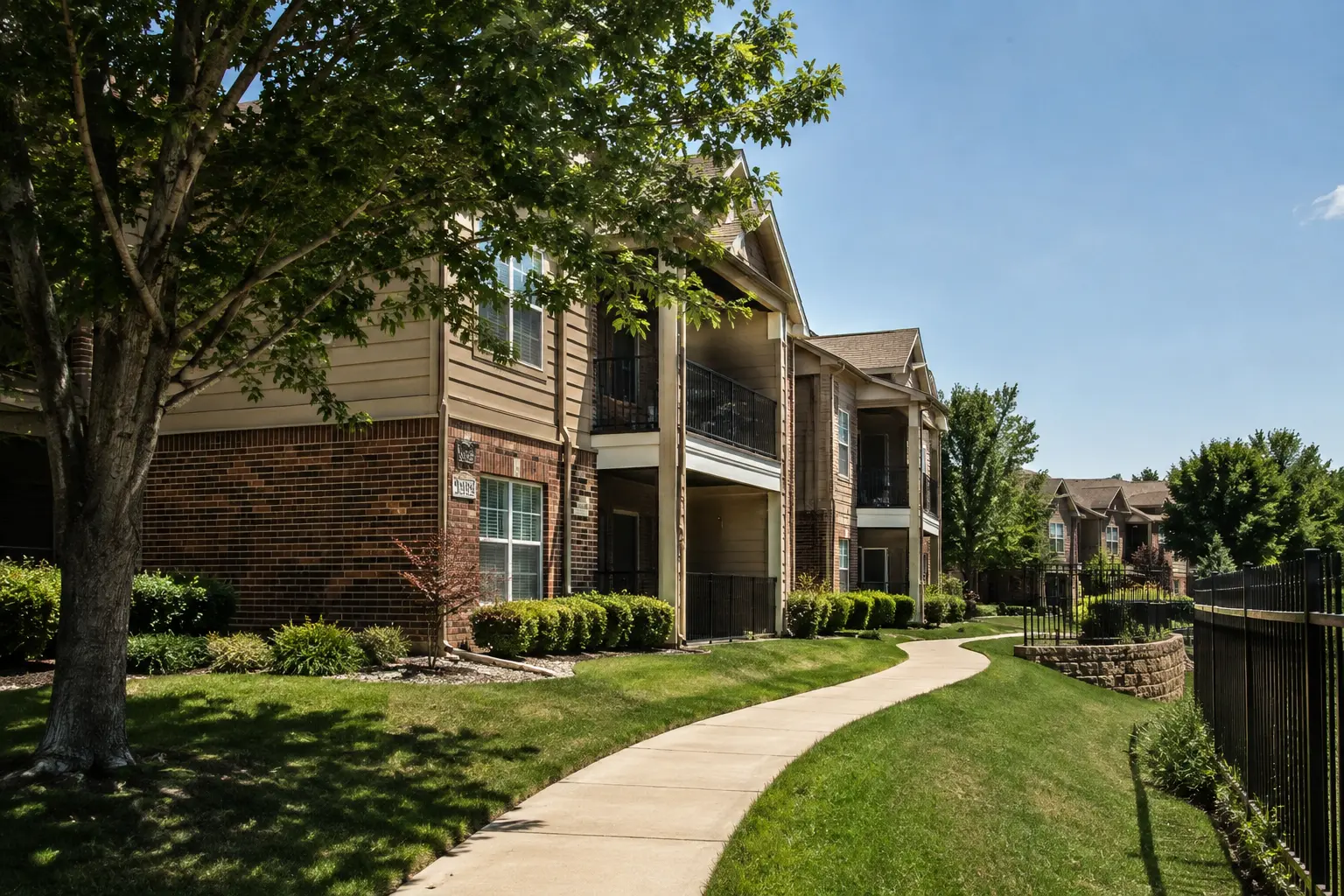 Realistic exterior view of Autumn Ridge Apartments in Tulsa, OK, featuring modern apartment buildings, landscaped lawns, mature trees, and a curved walking path.