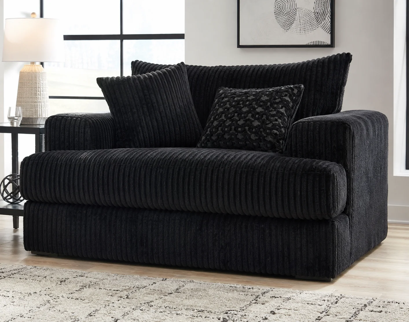 Ashley Midnight-Madness Chair and a Half in dark charcoal upholstery, styled in a modern living room with a decorative accent pillow.
